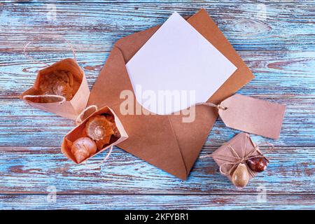 Draufsicht auf einen Umschlag mit Brief und Muscheln in Geschenktüten mit Platz für Grußtext, flach liegend. Stillleben auf einem hölzernen Hintergrund Stockfoto