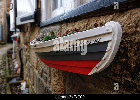 Rettungsboot geformter Blumentopf an einer Hüttenmauer in Robin Hoods Bay, North Yorkshire, Großbritannien Stockfoto