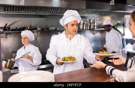 Serviceprozess im Café: Der Küchenchef serviert den Besuchern des modernen Restaurants Fertiggerichte Stockfoto