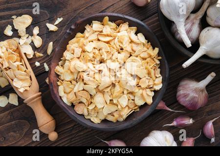 Schüssel mit getrockneten Knoblauchflocken, Knoblauchzehen. Knoblauchköpfe auf dem Küchentisch. Draufsicht, flach liegend. Stockfoto