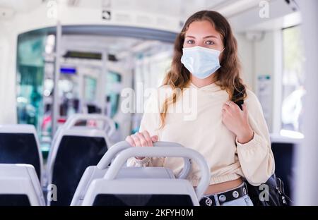 Porträt eines fokussierten Mädchens in einer Schutzmaske, das auf öffentlichen Verkehrsmitteln reitet Stockfoto