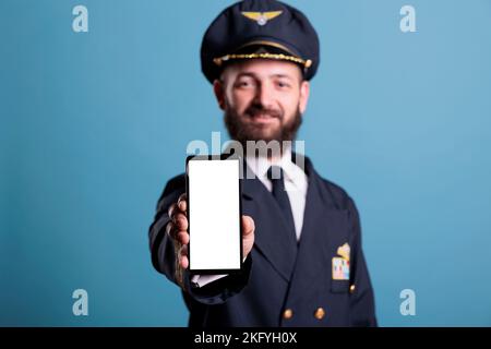 Flugzeugpilot zeigt Smartphone mit leerem weißen Bildschirm in Nahaufnahme, Handy-Werbung Produktmodell mit Kopierplatz. Flugzeugkapitän mit Telefon und leerem Display für App-Promo-Anzeigen Stockfoto