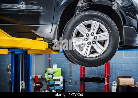 Fahrzeug in der Kfz-Werkstatt auf dem Lift angehoben. Nahaufnahme Des Rades. Planmäßige Mechanische Inspektion. Stockfoto