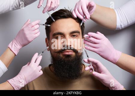 Hände von mehreren Ärzten, die Spritzen über das männliche Gesicht halten. Beauty und Kosmetologie Konzept. Kosmetische Verfahren Mesotherapie Stockfoto