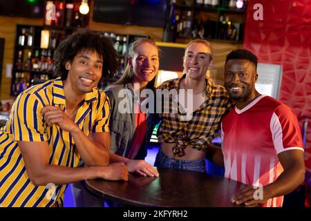 Porträt von vier verschiedenen männlichen und weiblichen Freunden, die in einer Bar vor der Kamera lächeln Stockfoto