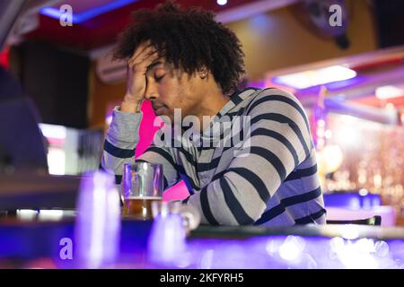 Betrunkener afroamerikanischer Mann, der seinen Kopf in der Bar hielt, mit einem Bier in einer Bar Stockfoto