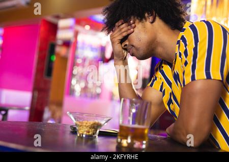 Deprimierter afroamerikanischer Mann, der an der Bar sitzt, mit einem Bier und seinen Kopf hält Stockfoto