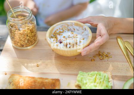 Unverkennbare Mutter und Kind, die im Park Joghurt mit Müsli zubereiten Stockfoto