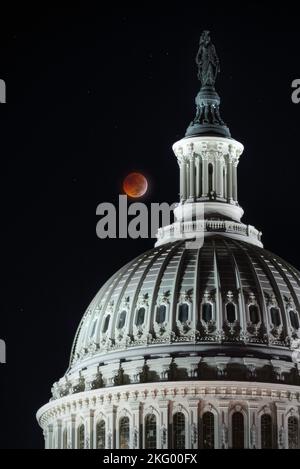 Eine totale Mondfinsternis vom 8.. November 2022 leuchtet seine bernsteinrote Farbe über der Kuppel des US-Kapitols. Stockfoto