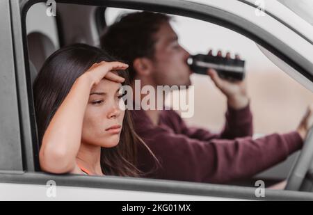 Betrunkenes fahrendes Paar verärgert müde vom Trinken im Auto. Mann Fahrer hält Bier Getränk am Lenkrad, wütend asiatische Frau Freundin schläfrig. Stockfoto