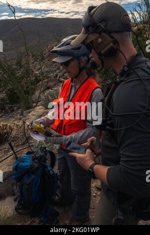 U.S. Marine Maj. Spencer Hart (rechts), ein AH-1Z Viper Pilot mit Marine Light Attack Helicopter Training Squadron (HMLAT) 303, Marine Aircraft Group 39, 3. Marine Aircraft Wing, Und Janene Colby, eine Tierbiologin am kalifornischen Department of Fish and Wildlife, geht darüber nach, wie man im Anza-Borrego Desert State Park, Kalifornien, am 16. Oktober 2022, mit einem Telemetriescanner Dickhornschafe aufspüren kann. HMLAT-303 Marineinfanteristen und staatliche, föderale und private Behörden nutzten die Möglichkeit eines externen Aufzugs über eine lange Leitung über UH-1Y Venom-Hubschrauber, um eine Wasserversorgung für gefährdete Dickhornschafe durchzuführen. Durch den Teppich Stockfoto