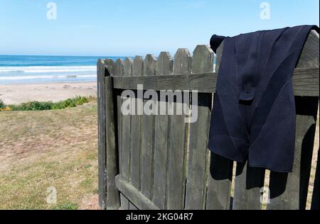 Ein kurzer Neoprenanzug hängt an einem Zaun, um zu trocknen, es hat Spaß im nahe gelegenen Meer. Stockfoto