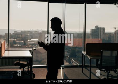 Silhouette eines Geschäftsmannes mit Telefon in den Händen im Büro stehend Stockfoto
