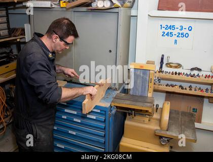 221018-N-ET093-1055 ADRIATISCHES MEER (18. Oktober 2022) Hull Maintenance Technician 1st Class Alex Smalley, aus Canano Island, Kalifornien, dem Flugzeugträger der Nimitz-Klasse USS George H.W. Bush (CVN 77) zugewiesen, reißt ein Plakat ab, 18. Oktober 2022. Die George H.W. Bush Carrier Strike Group ist auf einem geplanten Einsatz im US-Marinestreitgebiet in Europa stationiert und wird von der U.S. Sixth Fleet eingesetzt, um die Interessen der USA, Verbündeter und Partner zu verteidigen. Flugzeugträger, CVN 77, GHWB, US Navy, USS George H. W. Bush (CVN 77), Stockfoto