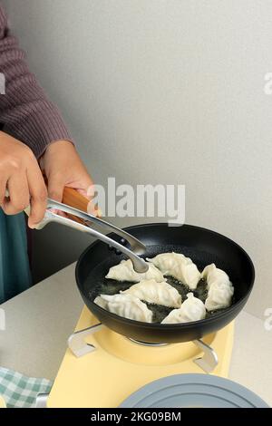 Weibliche asiatische Hand Kochen Gyoza Japanische Dumpling in heißem Öl mit Edelstahl Zangen Stockfoto