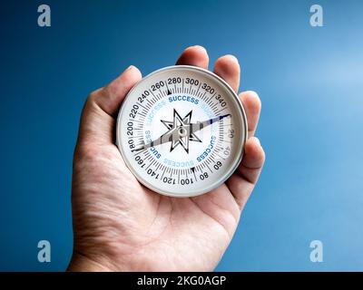 Nahaufnahme blaue Wörter „ERFOLG“ auf Kompass in der Hand eines Geschäftsmannes auf blauem Hintergrund. Geschäftsziel und Erfolg, Planungs- und Richtungskonzepte mit Ziel A Stockfoto