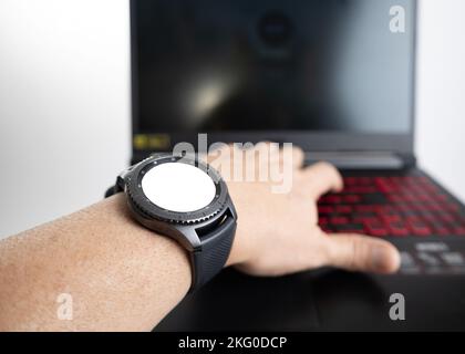 Männlicher Arm und Hand mit einer Smartwatch durch Tippen auf einem Laptop. Stockfoto