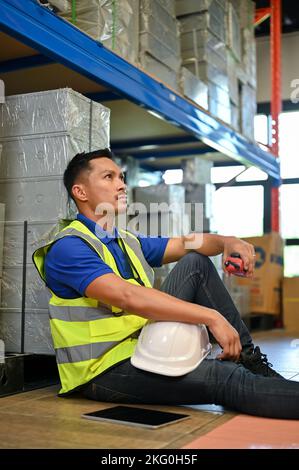 Portrait, müde Millennial asiatischen männlichen Lagerarbeiter sitzen im Lager. Industrie, Engineering. Stockfoto