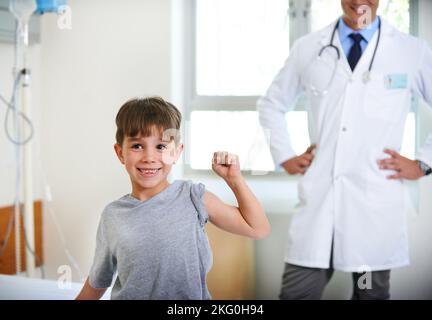 Der erste Platz für den stärksten Patienten. Ein entzückender Junge, der seine Armmuskeln im Krankenhaus beugt. Stockfoto