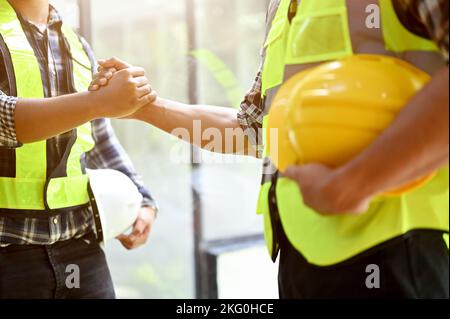 Professioneller asiatischer männlicher Ingenieur, der mit einem männlichen Bauleiter die Hände schüttelt. Teamarbeit von Industriearbeitern und Ingenieuren Stockfoto