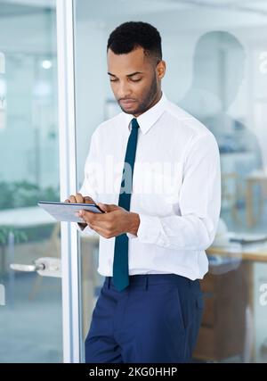Überprüfung der neuesten Geschäftszahlen. Ein hübscher junger afroamerikanischer Geschäftsmann, der sein digitales Tablet im Büro benutzt. Stockfoto