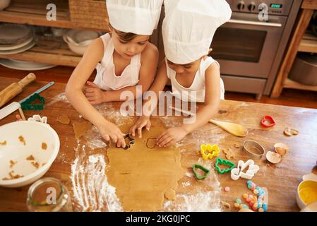 Familie, Backen und Kinder lernen, Kekse am Tisch zu Formen, entwickeln und binden in einer Küche. Kuchen, Cutter und junge Kinder, die Spaß beim Herstellen haben Stockfoto