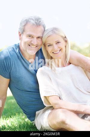 Sonnig am Tag im Park zusammen. Ein reifes Paar sitzt zusammen auf dem Gras. Stockfoto