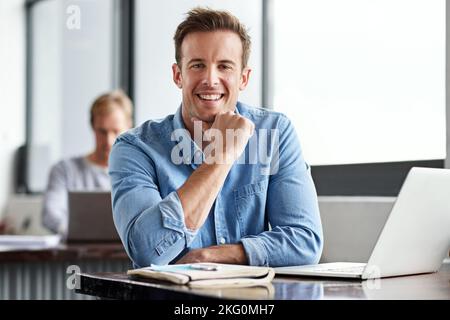 Wir halten es lässig in unserem Büro. Ein Mann, der in einem Büro an einem Laptop arbeitet. Stockfoto