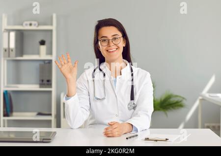 Freundliche Ärztin führt Online-Konsultationen mit Patienten, die vor der Webcam im Büro sitzen. Stockfoto