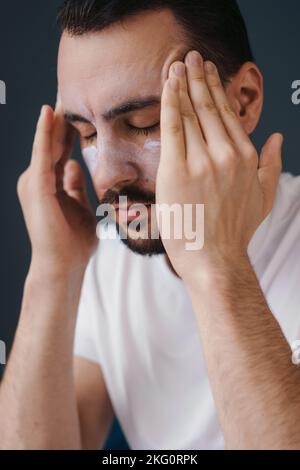 Nahaufnahme eines jungen bärtigen Mannes, der Gesichtscreme im Badezimmer aufträgt. Gesichtsbehandlung, Kosmetologie, Schönheitskonzept. Gesichtspflege. Konzept Stockfoto