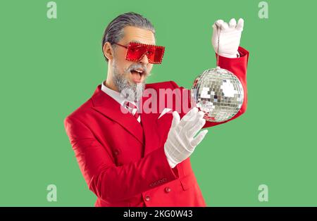 Extravaganter, lächelnder junger Mann in einem roten Anzug und weißen Handschuhen hält einen glänzenden Ball. Stockfoto