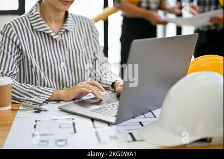 Schöne und professionelle junge asiatische Architektin oder Ingenieurin arbeitet an ihrem Schreibtisch, mit Laptop-Computer, sitzen im Büro. Zugeschnittenes Bild Stockfoto