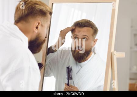 Schöner, eleganter Mann, der morgens vor dem Spiegel seine Haare kämmt und stylt. Stockfoto