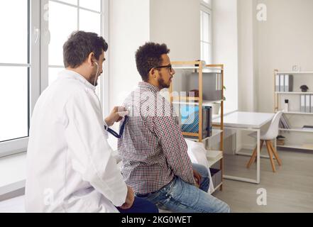 Während eines Arzttermins hört der Arzt mit Stethoskop auf die Lunge des Patienten, um zu Keuchen. Stockfoto