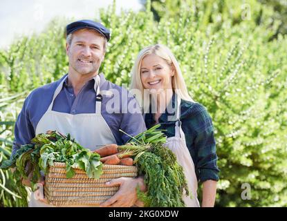 Frisch aus der Natur. Ein reifes Bauernpaar hält einen Korb mit frisch gepflücktem Gemüse. Stockfoto