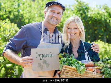 Es ist alles organisch. Ein reifes Bauernpaar hält einen Korb mit frisch gepflücktem Gemüse. Stockfoto