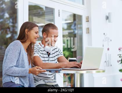 Von überall aus mit allem verbunden. Ein glückliches junges Paar, das vor einem Café zusammenarbeitet. Stockfoto