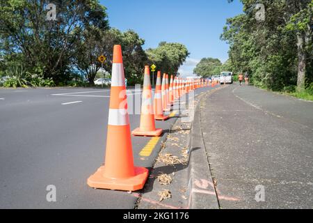 Orangefarbene Verkehrskegel entlang der Straße, verschwommene Menschen, die auf dem Fußweg laufen. Auckland. Stockfoto