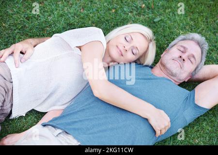 Intimität und Glückseligkeit. Ein reifes Paar, das auf dem Gras liegt und glücklich zu dir aufschaut. Stockfoto