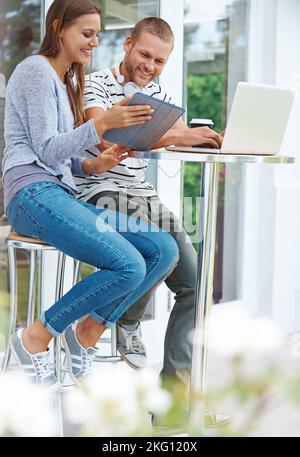 Schauen Sie sich diesen Status an. Ein glückliches junges Paar, das außerhalb eines Cafés zusammenarbeitet. Stockfoto