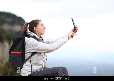 Seitenansicht Porträt eines glücklichen Trekkers, der ein Selfie im Berg macht Stockfoto