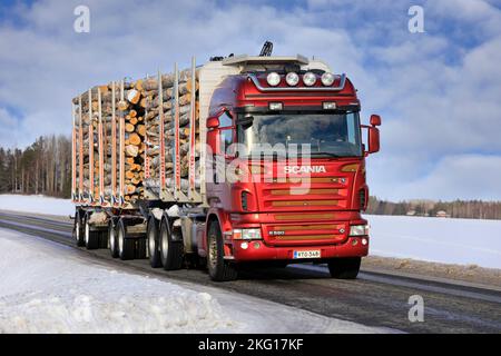 Red Scania R580 Holzlader vor einem Holzanhänger voller Birkenstämme auf der Landstraße im Winter. Salo, Finnland. 12. Februar 2022. Stockfoto