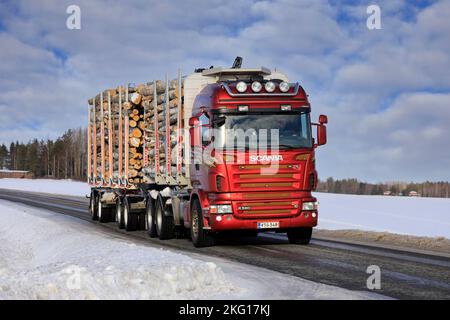 Red Scania R580 Holzlader vor einem Holzanhänger voller Birkenstämme auf der Landstraße im Winter. Salo, Finnland. 12. Februar 2022. Stockfoto