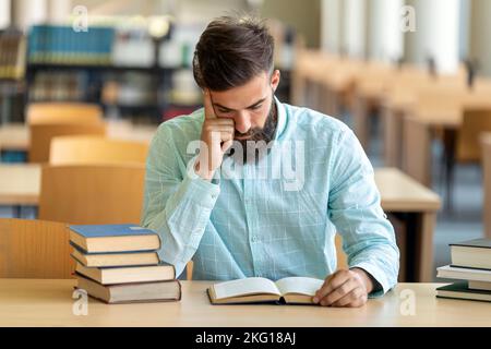 Erschöpfter junger Mann studiert und bereitet sich auf die Prüfung in der Universitätsbibliothek vor. Bildung Menschen Konzept Stockfoto