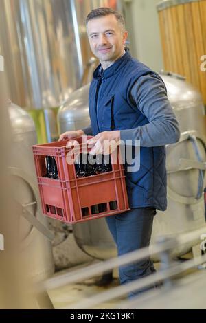 Porträt eines Arbeiters, der eine Kiste Bier in der Brauerei trägt Stockfoto