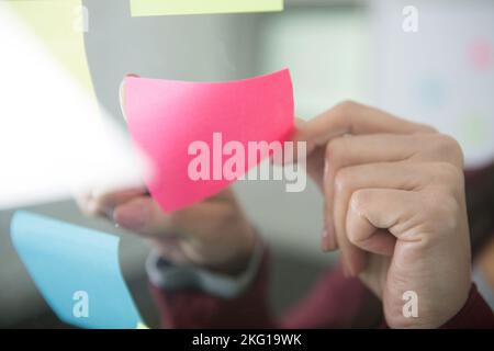 Nahaufnahme der Hände, die Notizen an der Glaswand kleben Stockfoto