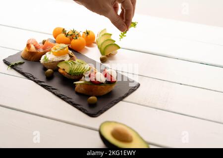 Zubereitung von Sandwiches, Zubereitung von Crostini, Canape, Antipasti mit Lachs Avocado, Tomaten, Frischkäse, Mozzarella für Party, Geburtstag. Das Konzept der gesunden Ernährung und der mediterranen Küche. Stockfoto