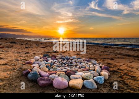 Während des Sonnenuntergangs am Strand werden heilige Ritualsteine für spirituelle Zeremonien in Einem Kreis angeordnet Stockfoto