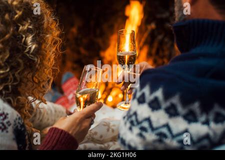 Rückansicht des Paares genießen und feiern zusammen mit Champagner-Flöten im Haus mit Kamin im Hintergrund klirren. Winterurlaub Saison A Stockfoto