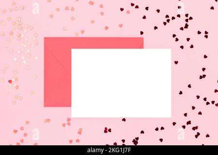 Leeres weißes Papiermockup, Umschlag und rote Herzen Konfetti auf einem rosa Hintergrund. Kreatives Konzept. Stockfoto